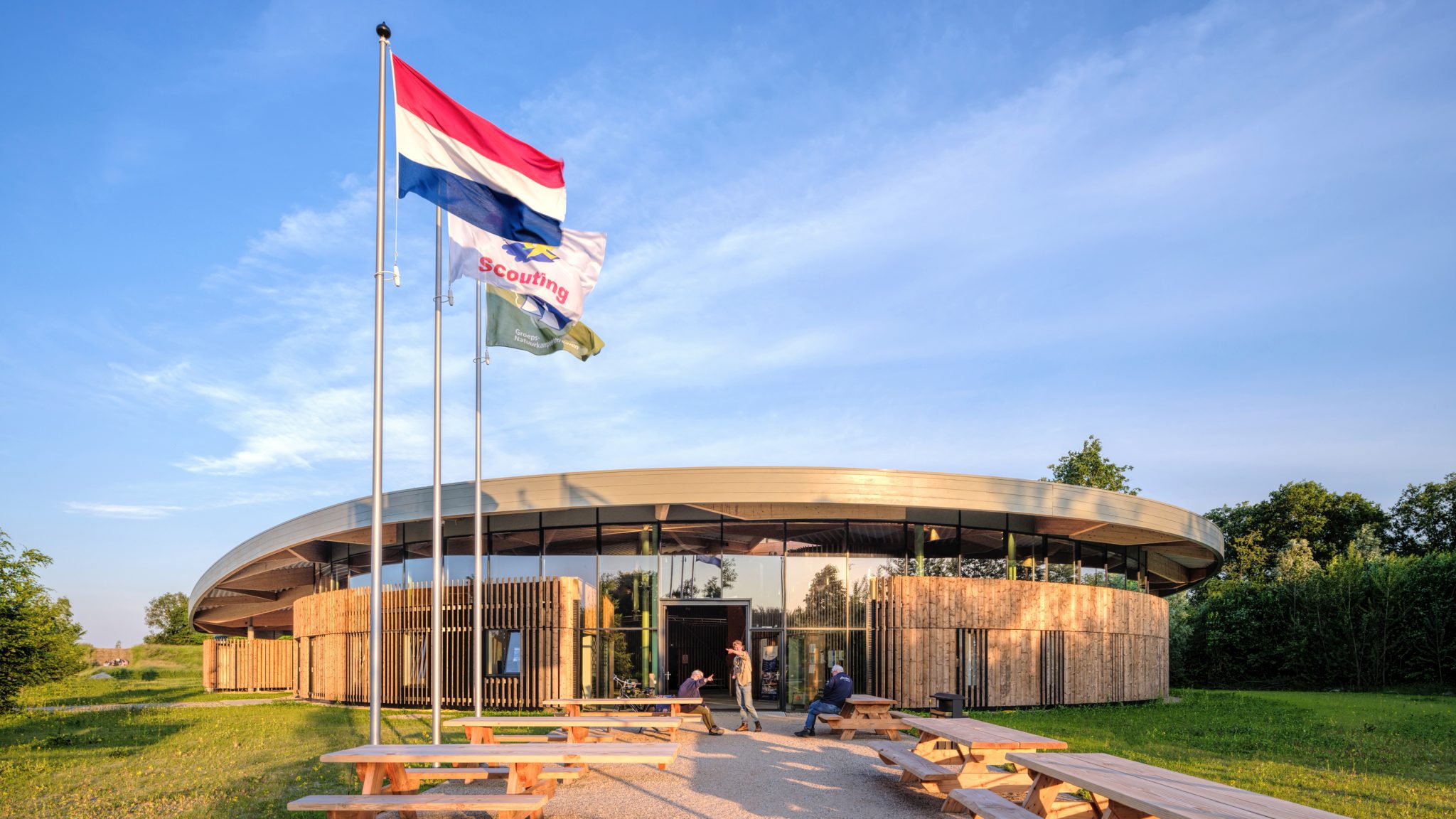 Main entrance approach of the Avonturenhuis Scoutinglandgoed Zeewolde, wooden facade and laminated curved wooden roof with blue sky and building in nature